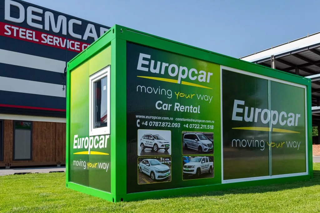 Container comercial verde Europcar cu grafică publicitară și fotografii de mașini, la sediul DEMCAR