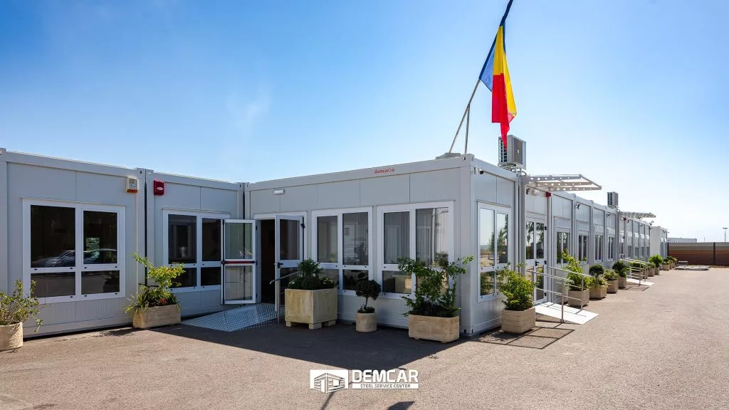 Construcție modulară amplă cu drapelul României, intrare vitrată și rampă de acces