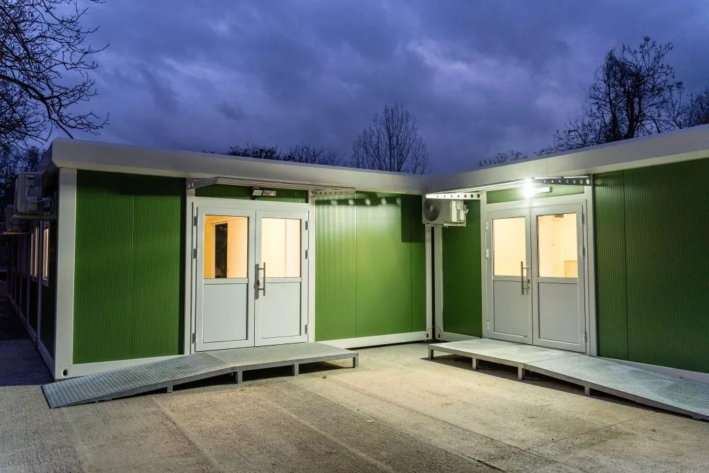 Construcție modulară verde cu uși de intrare și rampe de acces, fotografiată în lumina serii