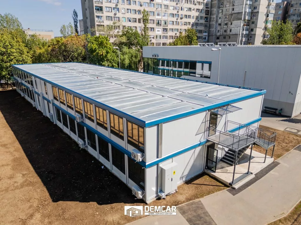 Vedere aeriană a unei construcții modulare cu două etaje, scară metalică exterioară și acoperiș cu luminatoare
