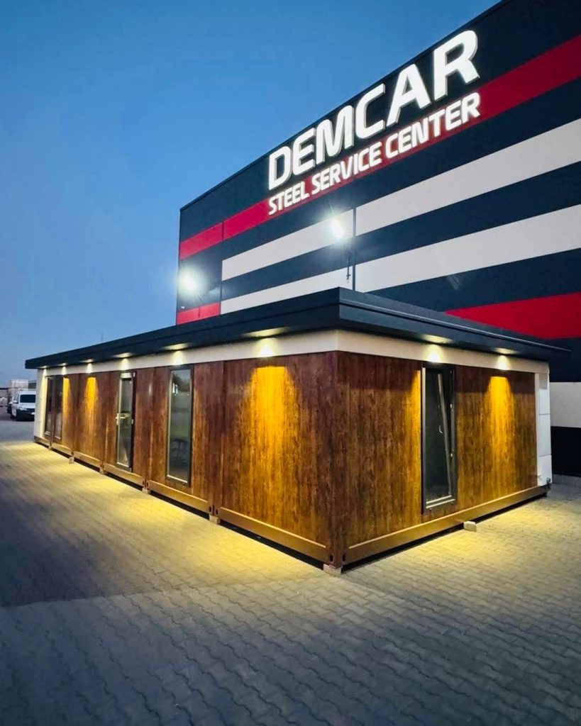 Construcție modulară cu placare din lemn iluminată seara în fața sediului DEMCAR